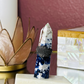 blue and white (uv reactive) blue sodalite sits on a blue flash moonstone base handcrafted into a crystal ring holder fitting ring sizes 6.5 and bigger. sits on beside table with india marble box and lotus candle holder