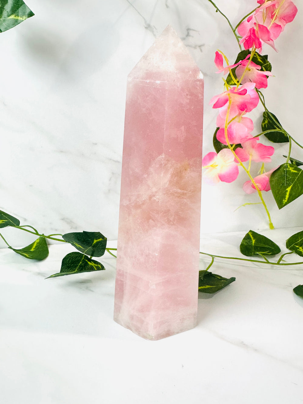 large rose quartz tower on marble with leaves and flowers