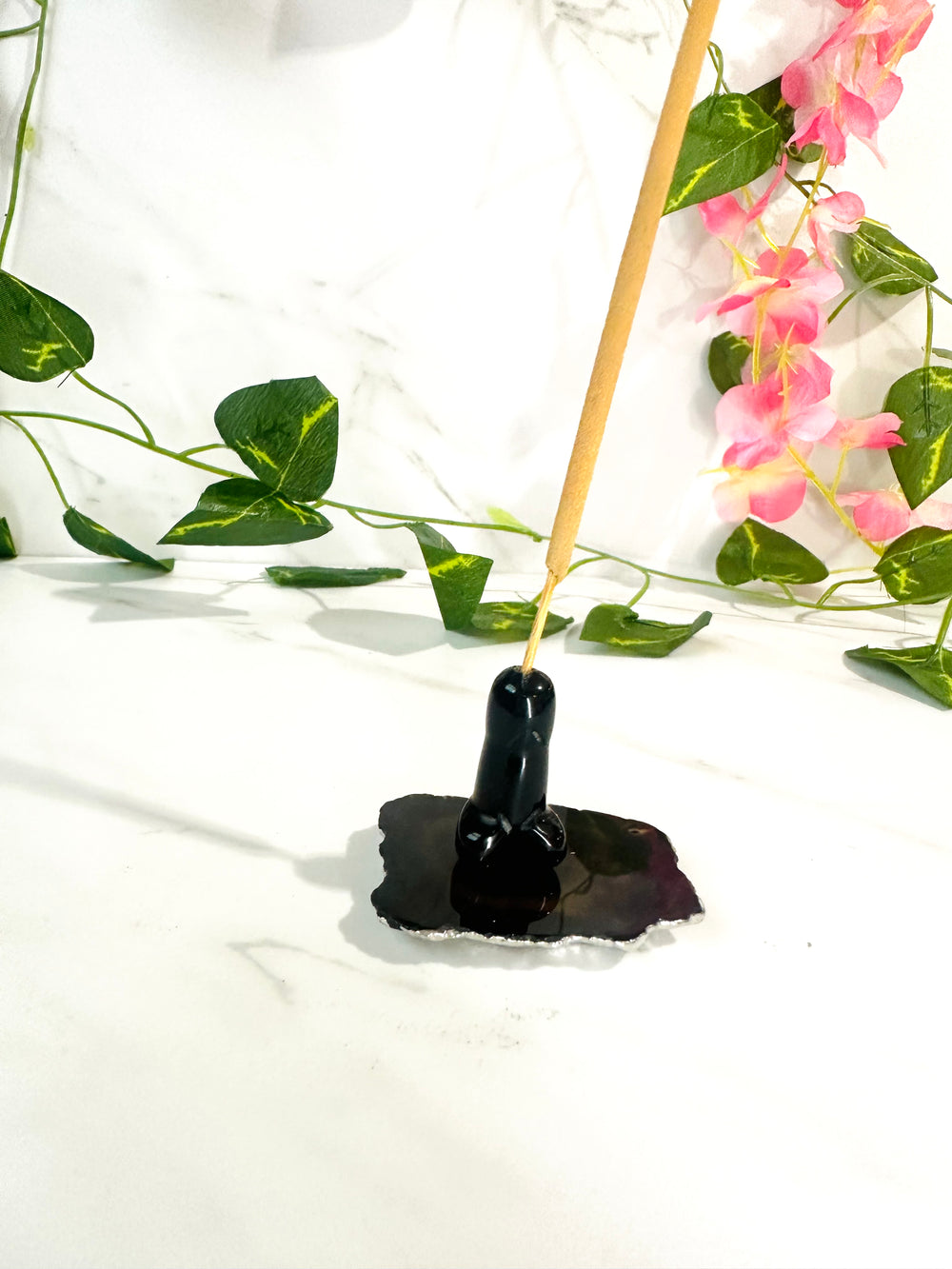 black obsidian phallic incense holder on white marble with leaves and flowers