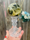 prehnite sphere with black tourmaline. sitting on glass stand outside