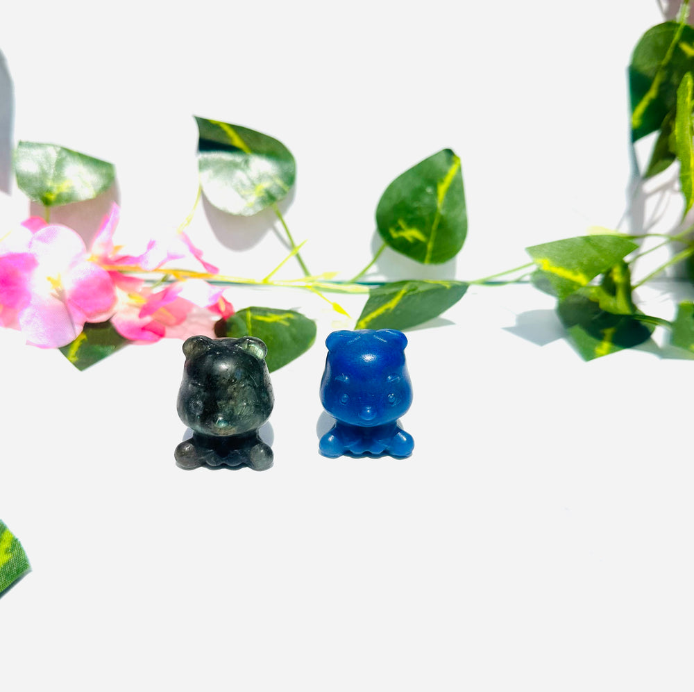 crystal carved teddy bear. lapis lazuli and labradorite. sitting on white marble surrounded by vines and flowers. 