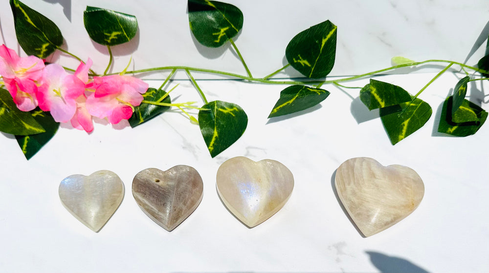 blue flash moonstone hearts sits on white marble with vines and greenery.