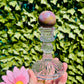 pink yellow and blue ocean jasper sphere being held by hand with crystal sphere holder in front of greenery