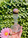 pink yellow and blue ocean jasper sphere being held by hand with crystal sphere holder in front of greenery