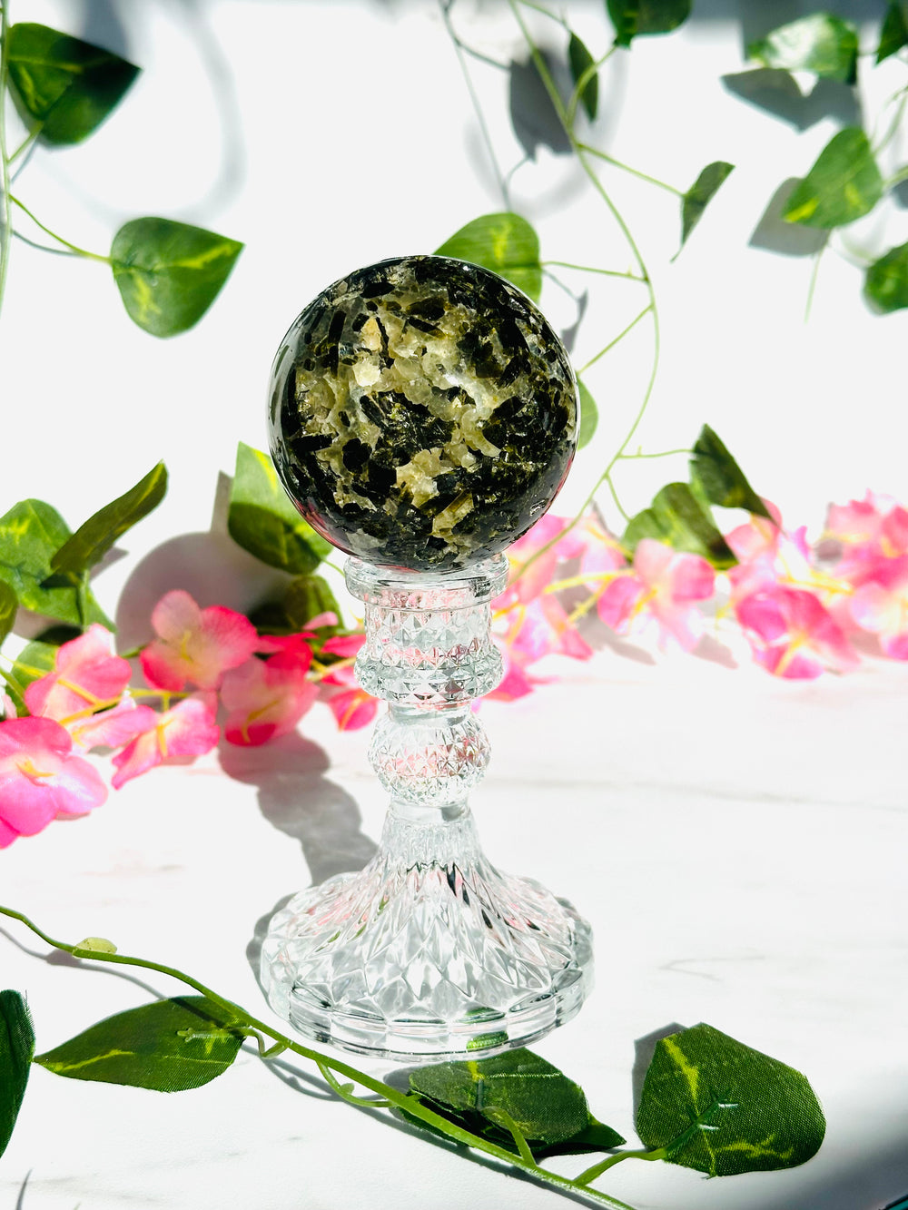 prehnite sphere with black tourmaline. sitting on glass stand surrounded by vines and flowers