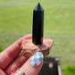 black obsidian tower sits upon a redish petrified base handcrafted into a crystal ring holder. video spinning ring holder in front of green field.. ring holder fits ring sizes 4 and larger