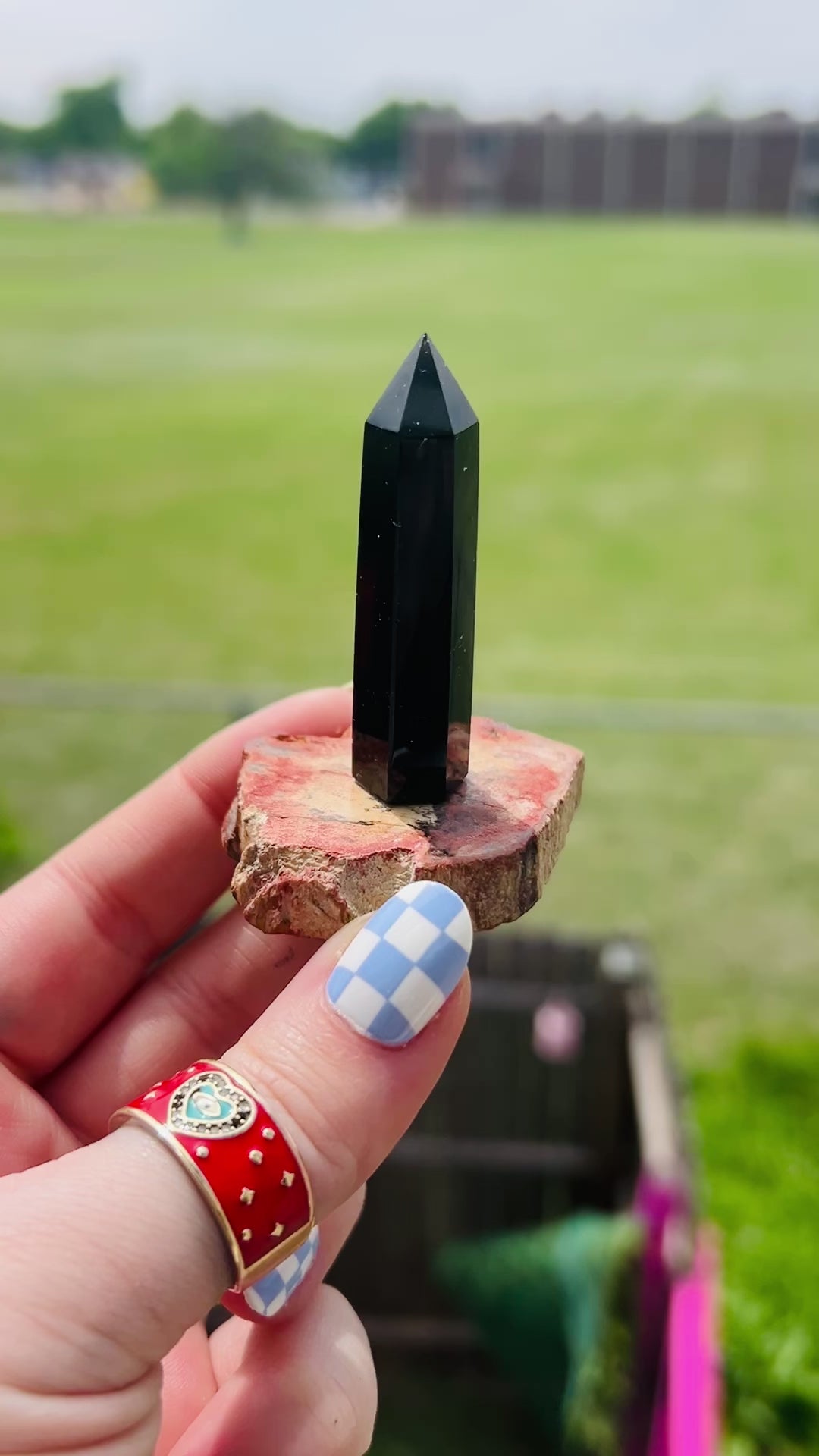 black obsidian tower sits upon a redish petrified base handcrafted into a crystal ring holder. video spinning ring holder in front of green field.. ring holder fits ring sizes 4 and larger