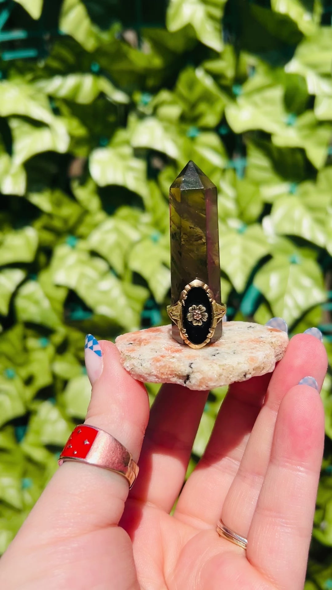 smokey quartz tower sits on a sunstone smokey quartz base. the handcrafted crystal ring holder is held in front of greenery and fits ring sizes 5 and bigger. 