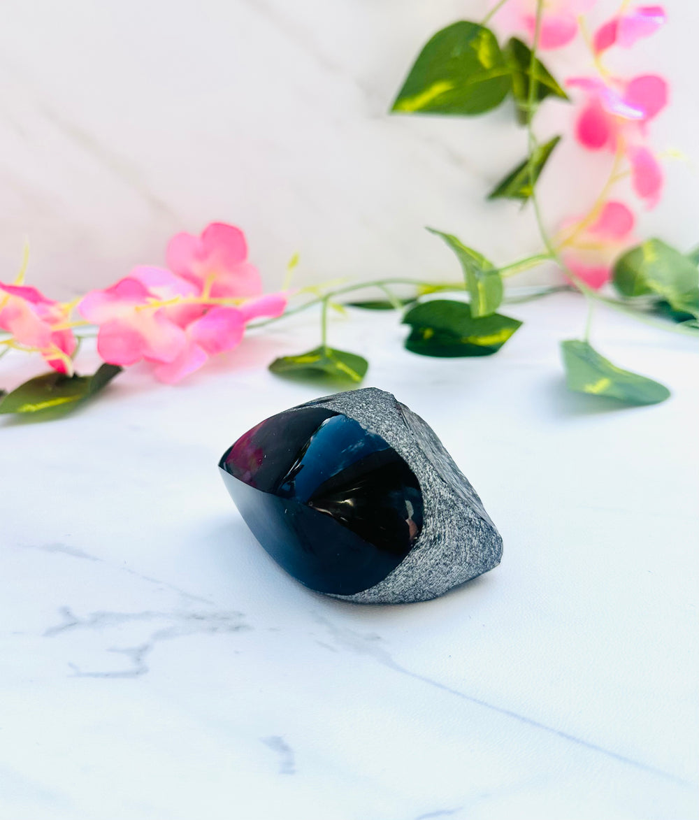 raw rainbow obsidian with polished front sitting on white marble with vines and flowers