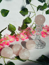 multiple rose quartz spheres sit on white marble in front of greenery and flowers