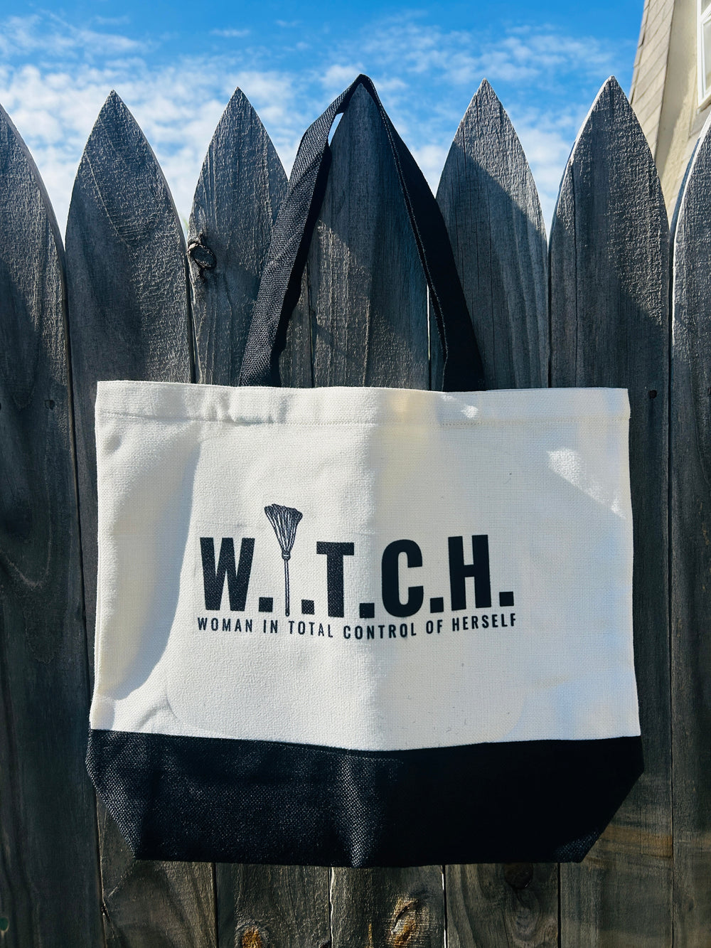 tote bag that says w.i.t.c.h. woman in total control. hanging on a fence